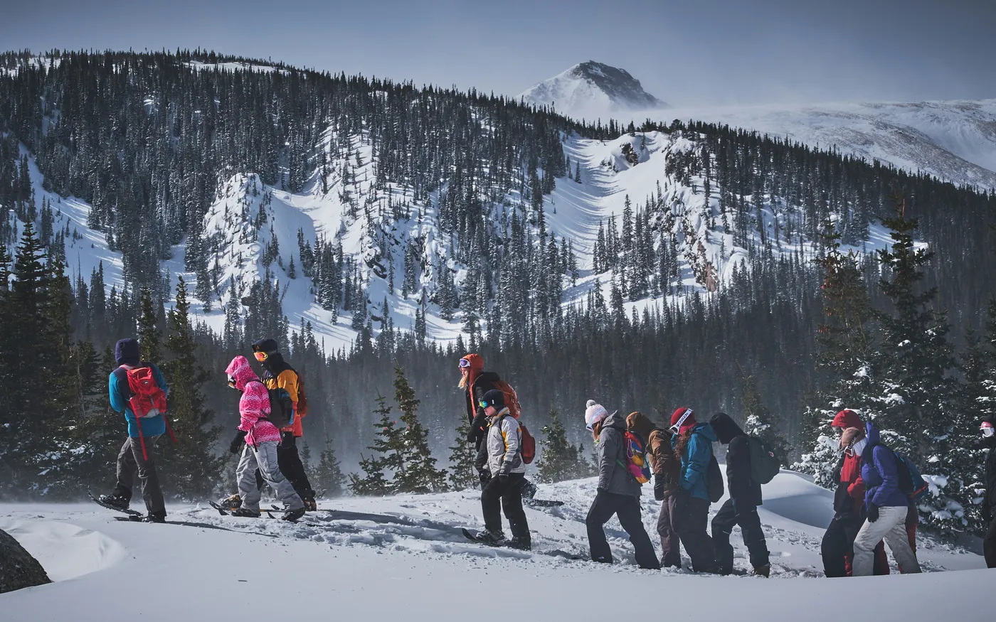 Line of snowshoe hikers traversing open snow beneath snow-covered mountains